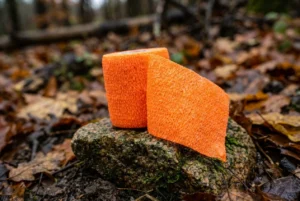 Bright orange High-Visibility Cohesive Bandage roll on a rocky terrain background for search and rescue gear