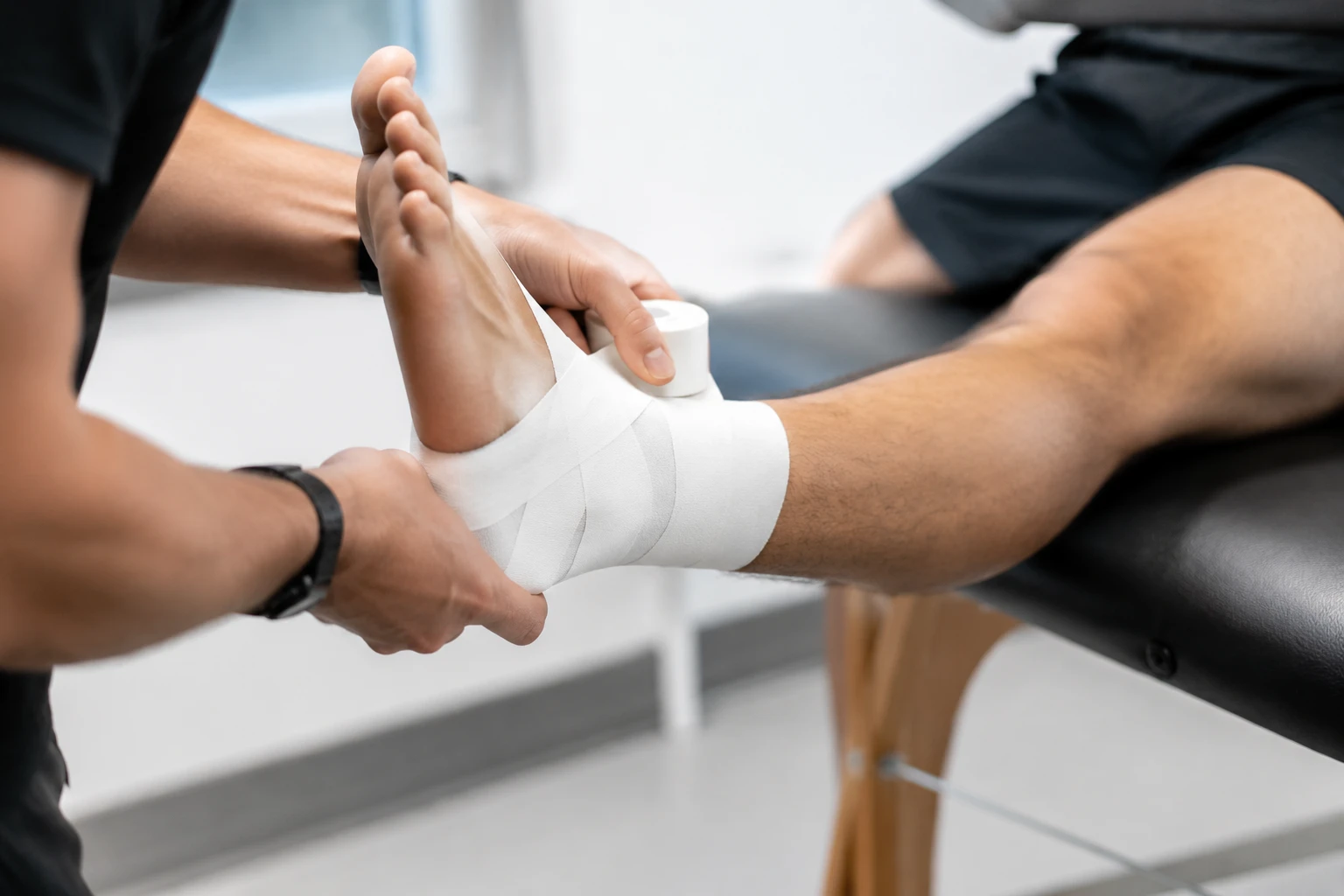Professionelle Anwendung von unelastischem Sporttape aus dem Großhandel am Sprunggelenk eines Sportlers zur Demonstration der korrekten Technik für die Gelenkunterstützung